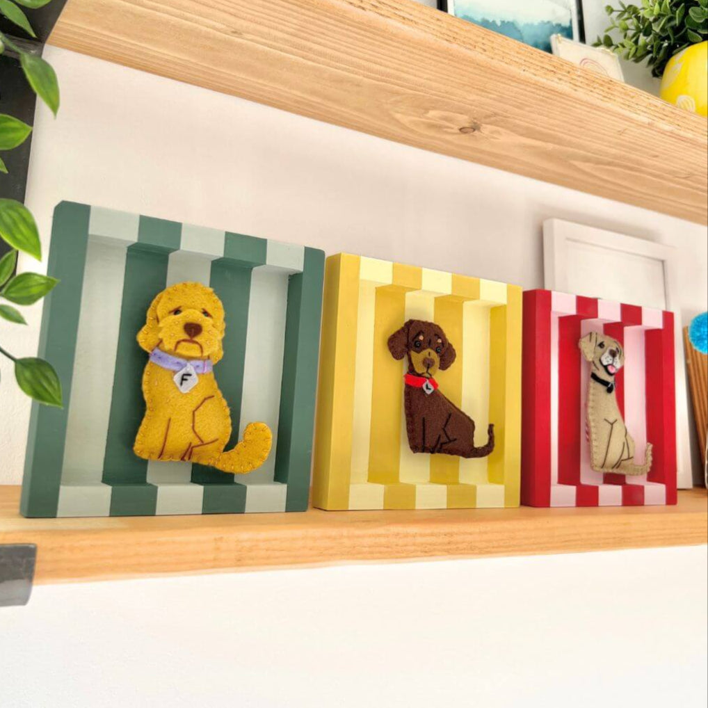 All 3 coloured frames displayed together on a shelf Each hasve a felt dog ornament inside.