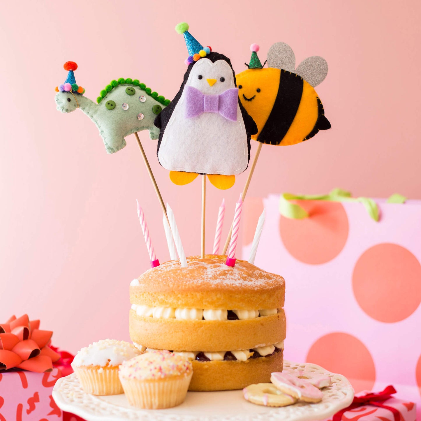 Felt animal cake toppers, dinosaur, penguin and bee arranged on a birthday cake