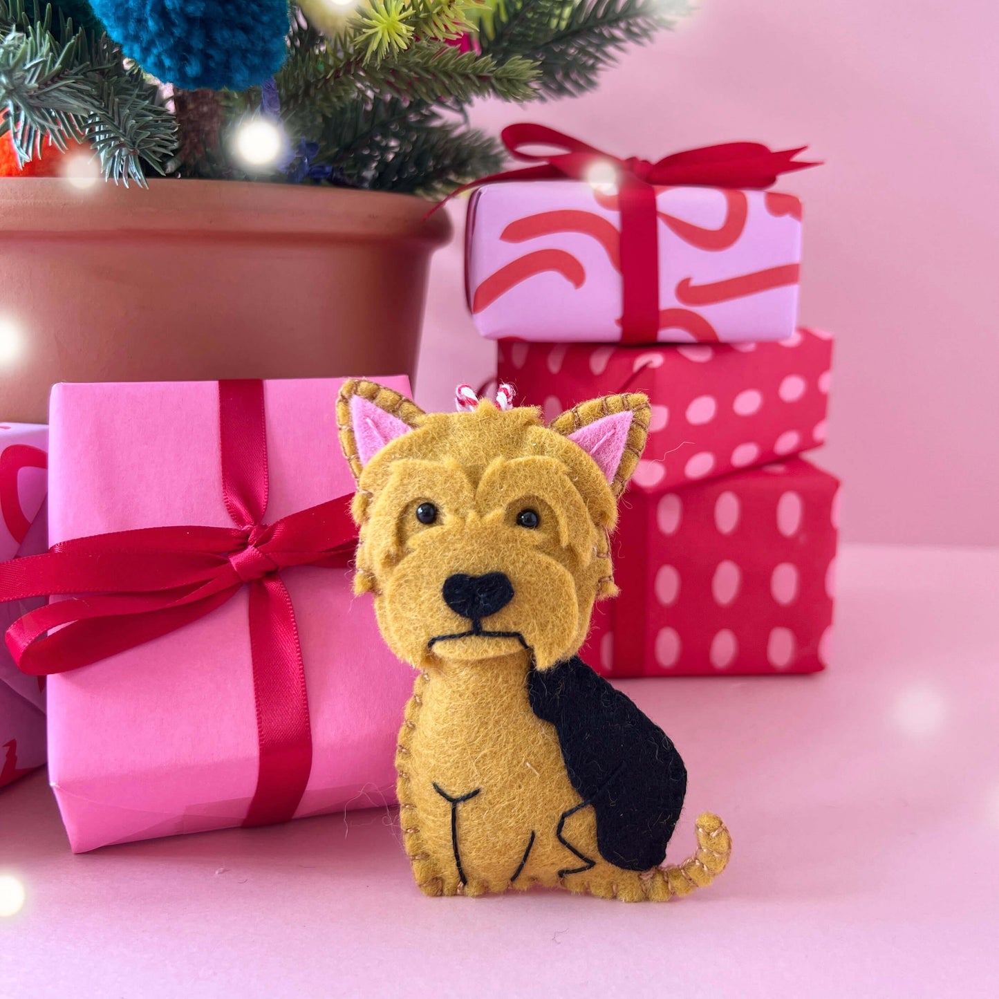 A yorkshire terrier custom dog ornament in black and tan. The ornament is displayed next to a Christmas tree and gifts to show it's purpose.