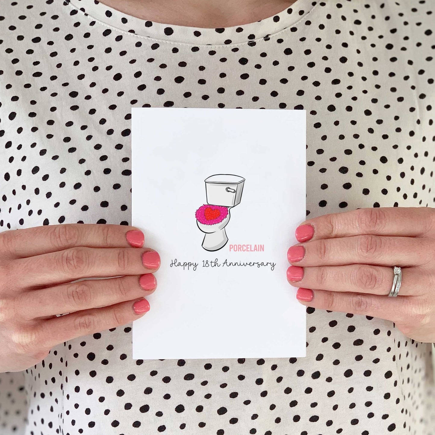 A person holding a 18th anniversary card. On the card is a drawing of a toilet as it's a porcelain anniversary.