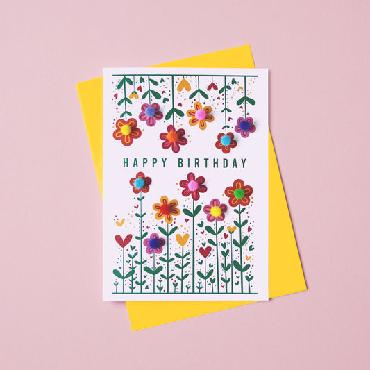 Birthday card with colourful flowers and decorated with pom pom. Th e birthday card says Happy Birthday