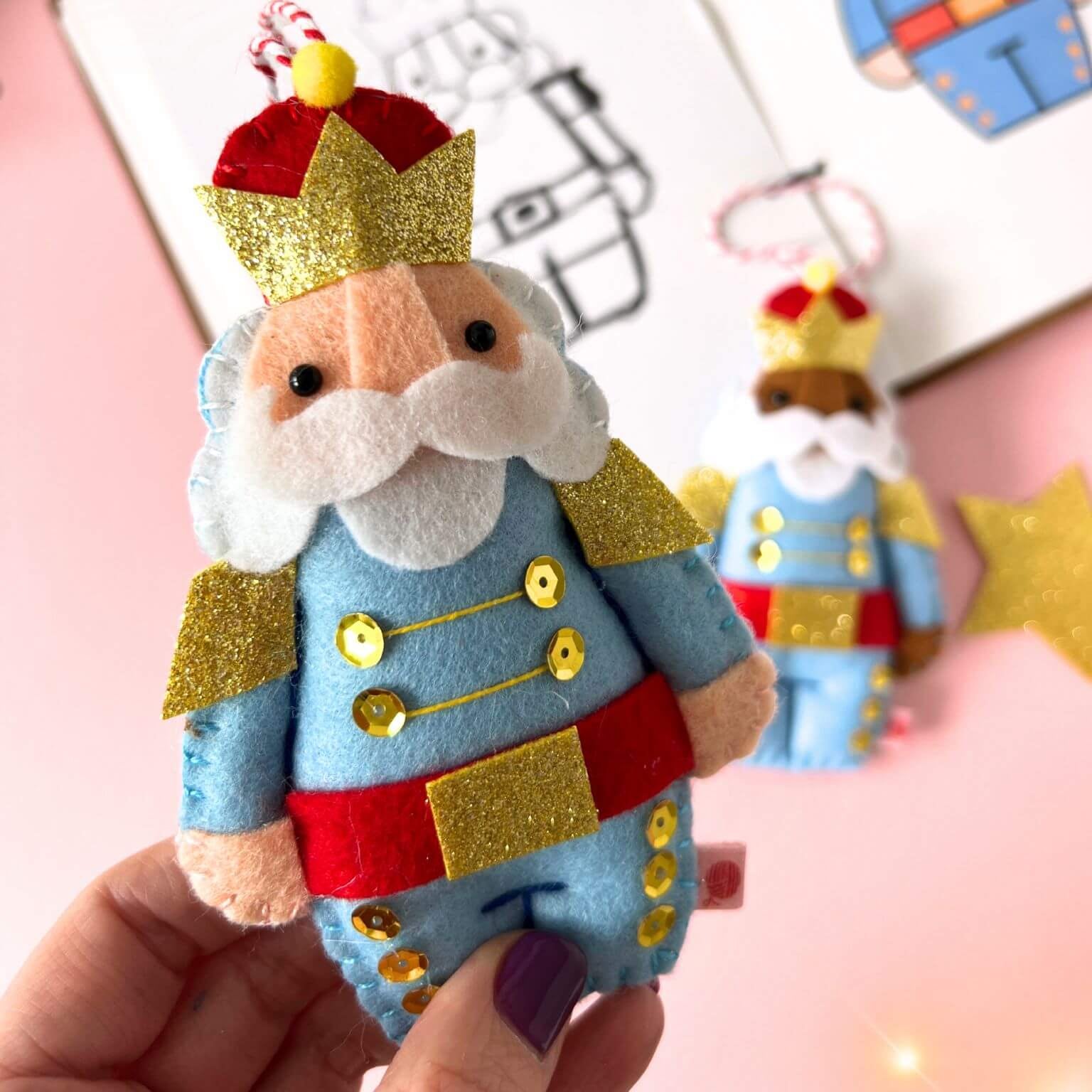 Nutcracker ornament. Handmade from felt with lots of gold sparkle. In the background are the sketches for the design.