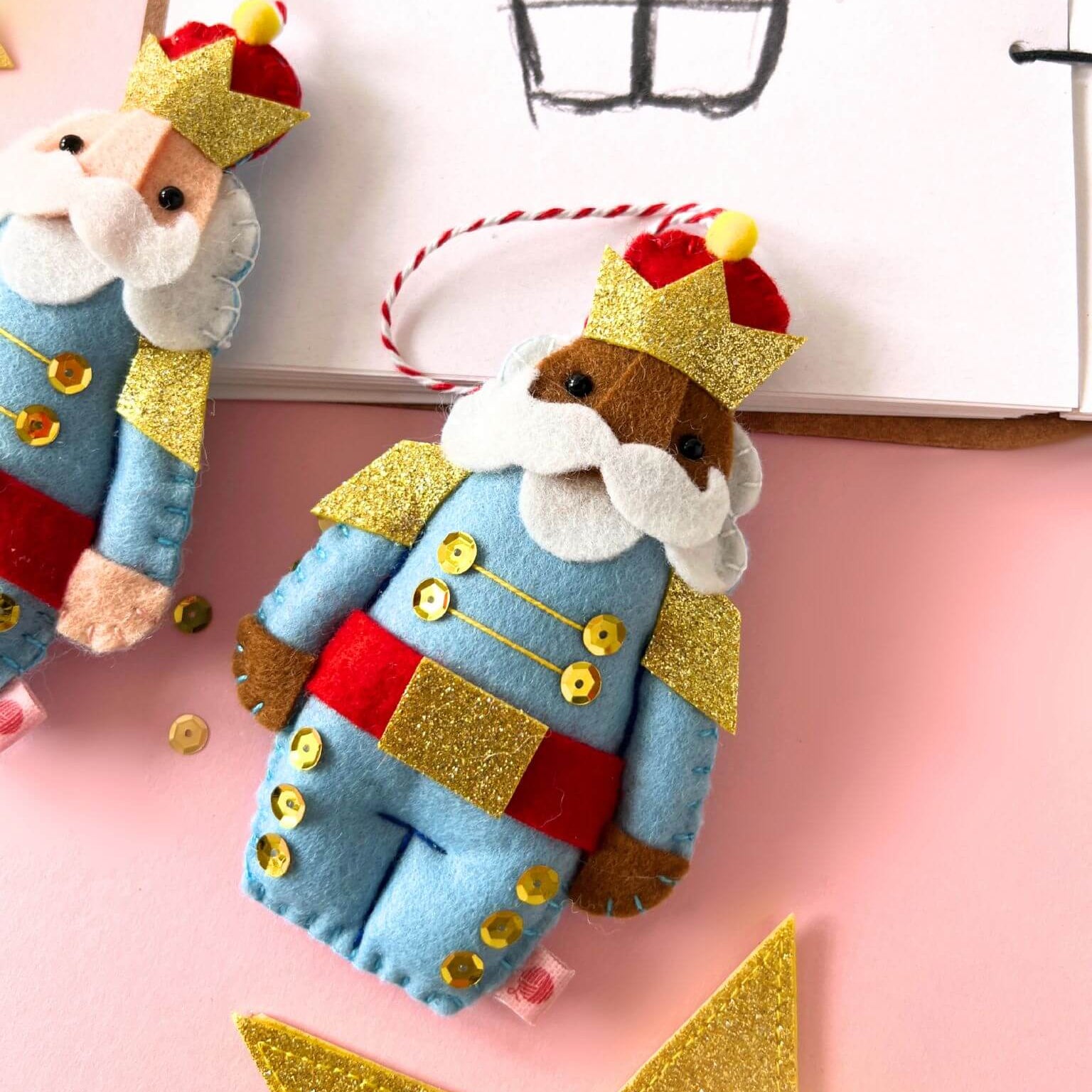 Decorative felt nutcracker ornaments  on a pink background with a star.