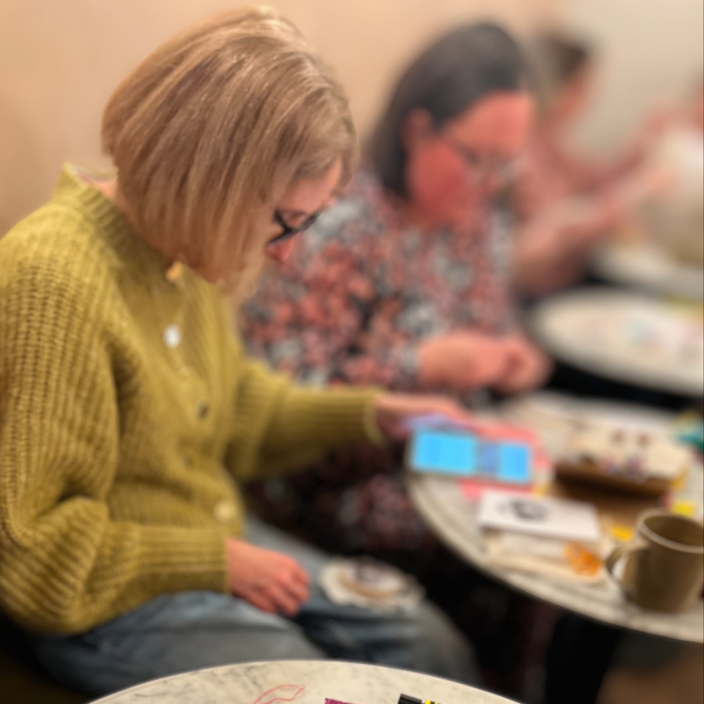 People sitting around a table with various items including a teacup, snacks, and a phone.