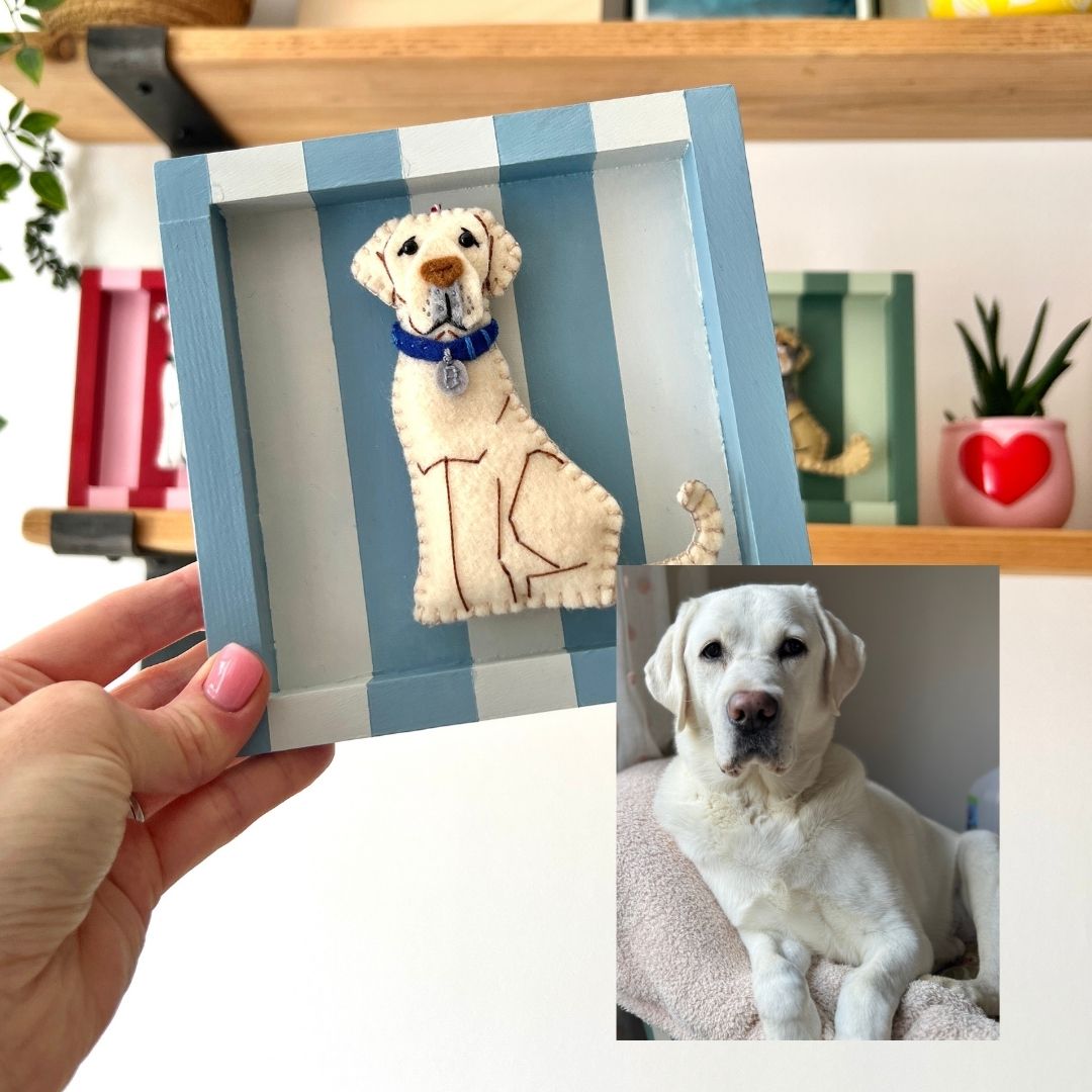 A hand holds a custom felt Labrador Retriever portrait in a blue striped shadow box frame. An inset photo in the bottom right corner shows the real dog used as the reference. Created by Miss Shelly Designs.