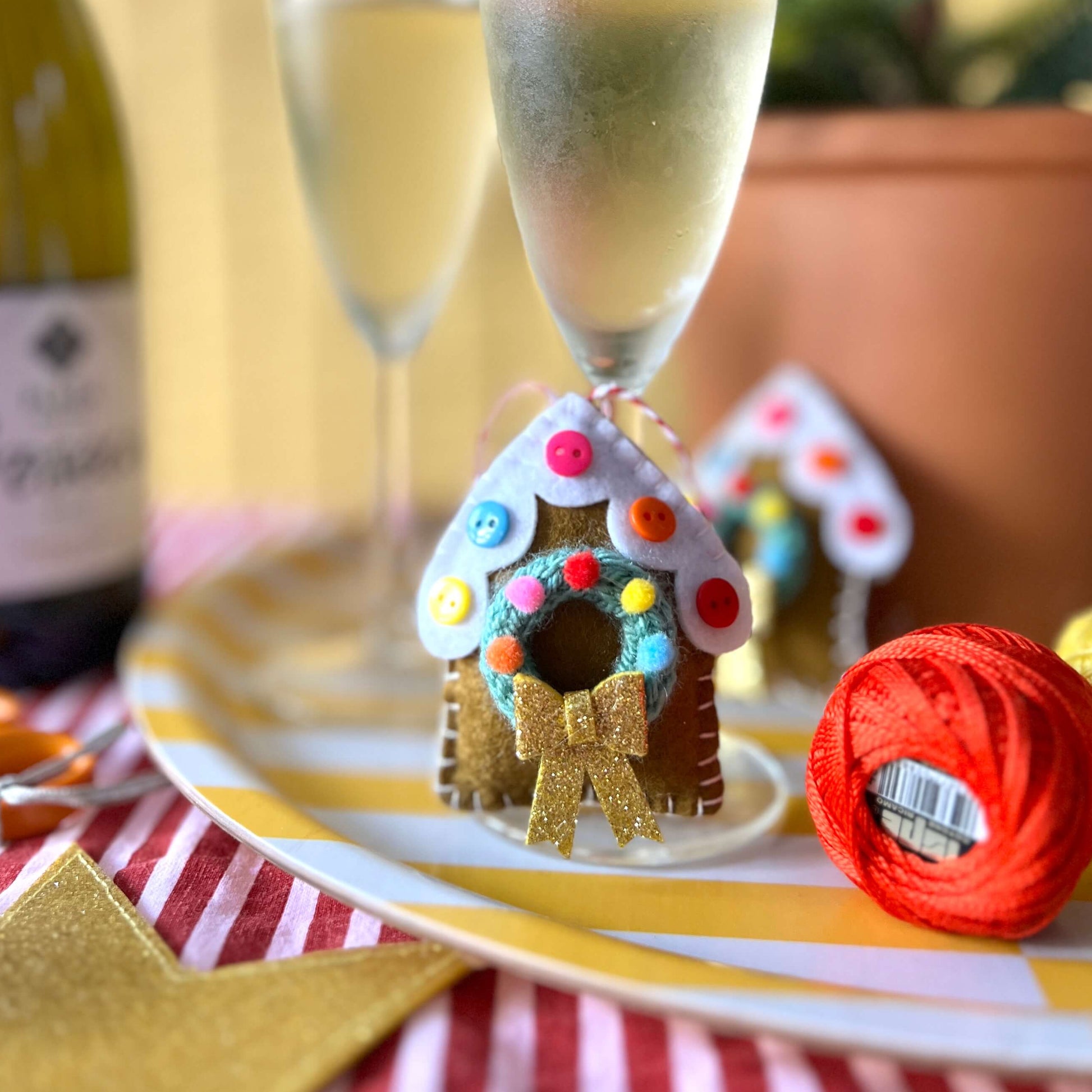 Decorative gingerbread house on a plate with champagne glasses and a bottle in the background.