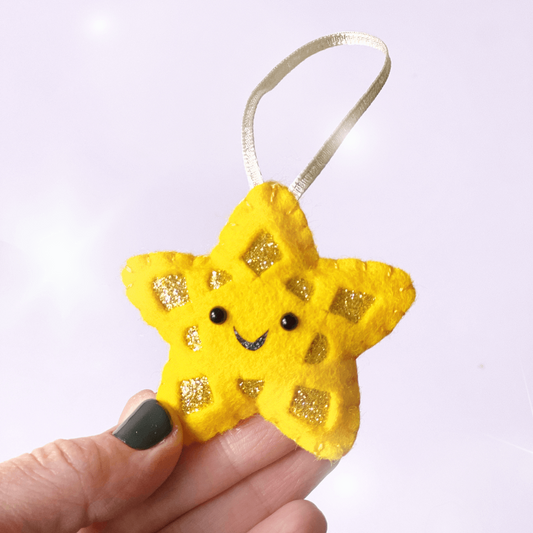 A hand holding a gold Christmas star. The star has a happy face