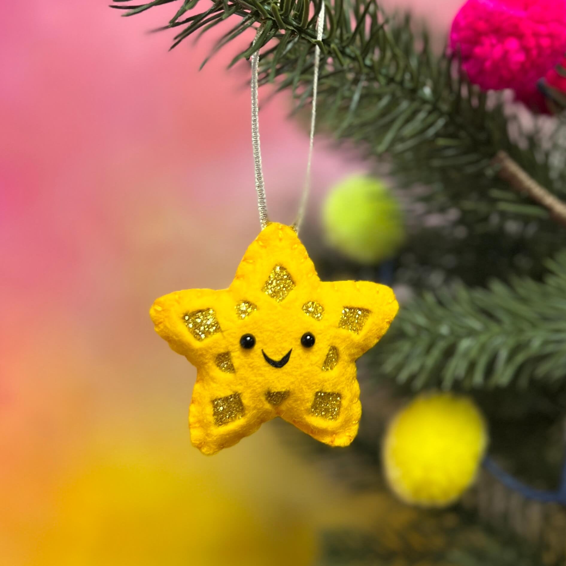 Yellow star with happy face hanging from a Christmas tree.