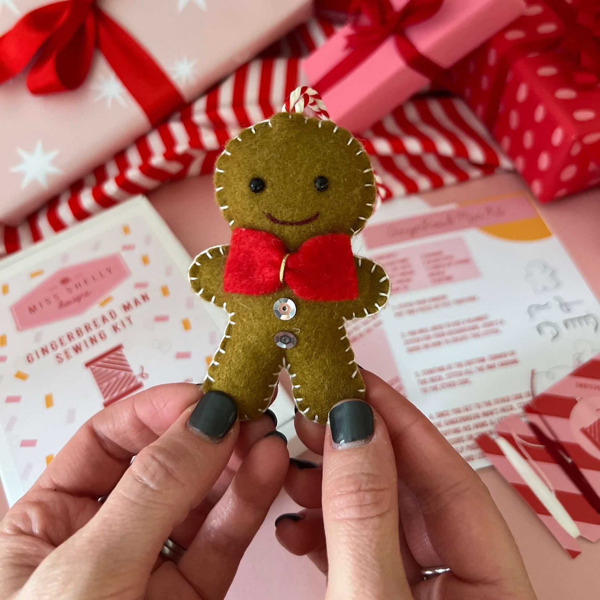 Felt gingerbread man ornament held by hands with Christmas presents in the background
