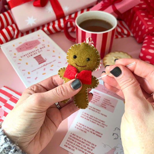 Person holding a felt gingerbread man ornament with a red bow tie, surrounded by Christmas-themed items.
