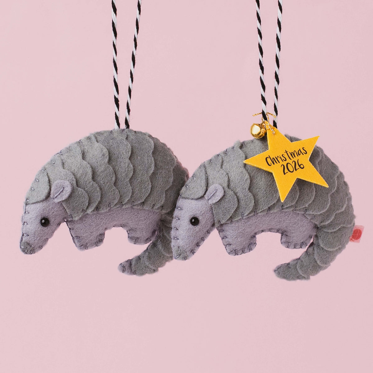 Two handmade grey felt pangolin Christmas ornaments with individually layered felt scales and black bead eyes, one with a yellow personalised star tag.