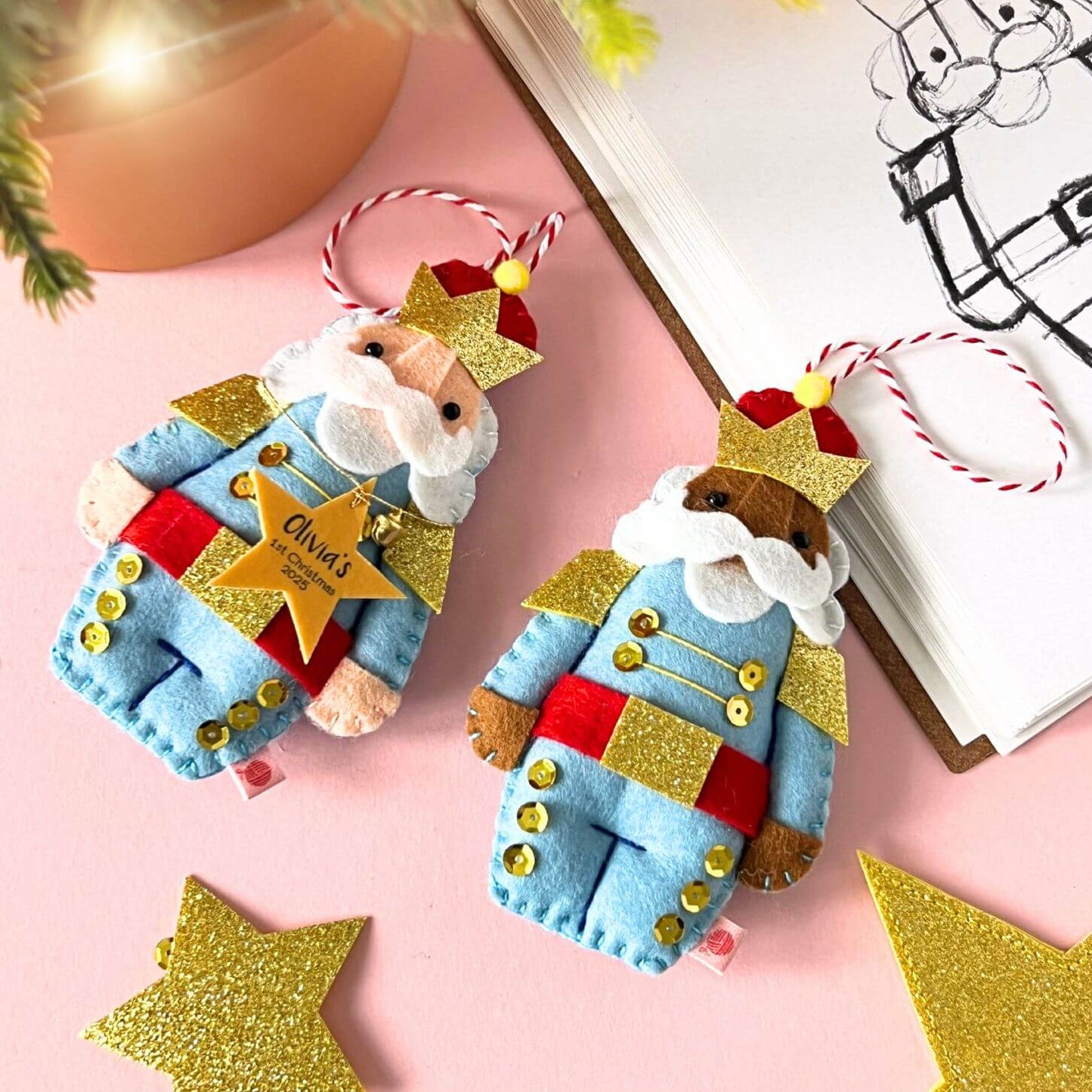 Two nutcracker Christmas ornaments, rested on a pink background.