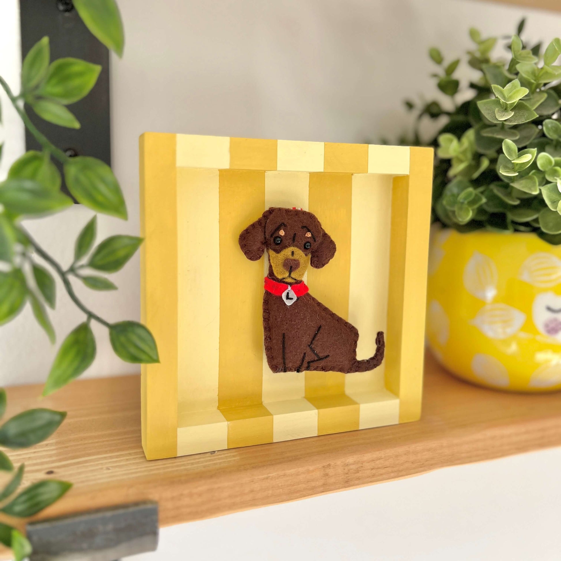 A yellow striped frame with a chocolate and tan Dachshund sitting in the middle. The frame is displayed on a shelf.