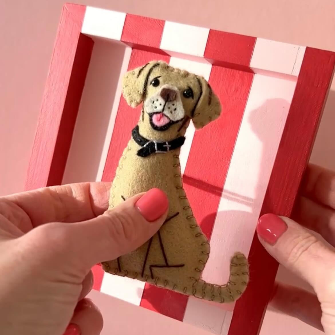 A golden felt dog ornament being removed from a red and pink striped frame. It can now be used as a hanging ornament.