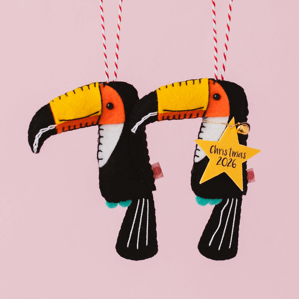 Two handmade black felt toucan Christmas decorations with bright yellow and orange beaks and embroidered details, one with a personalised Christmas 2026 star tag.