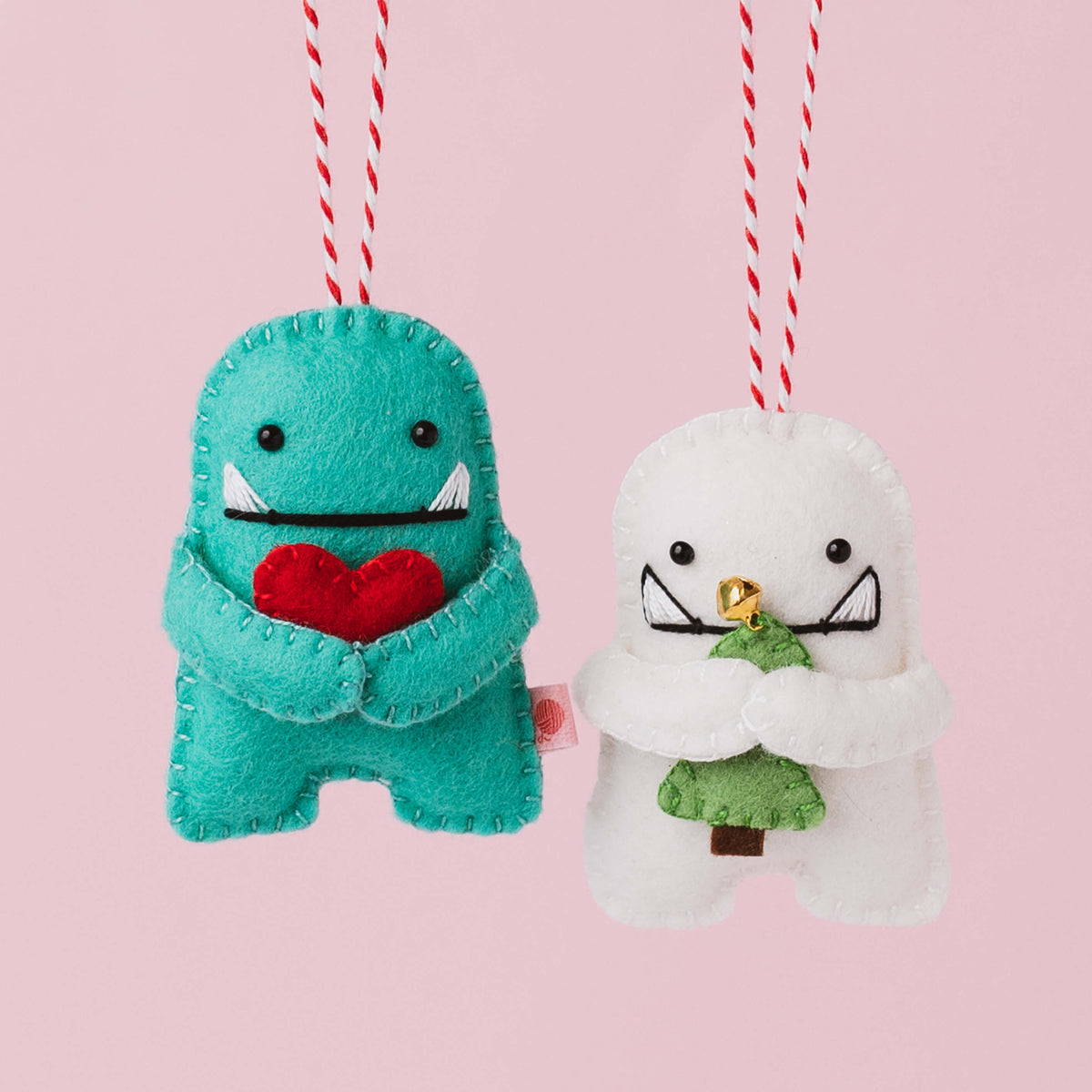 Handmade white  and green felt Christmas Hug Monster decoration with black eyes, embroidered smile and little arms hugging a green felt Christmas tree or red heart.
