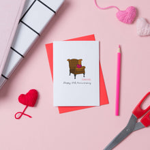 Load image into Gallery viewer, 17th anniversary card with a picture of a leather armchair on the front. The card is placed on a red envelope and has some hearts, scissors and a pencil next to it.