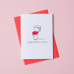 a 18th anniversary card with a picture of toilet on the front. Next to the toilet is the text - porcelain and Happy 18th Anniversary. The card sits on a red envelope.