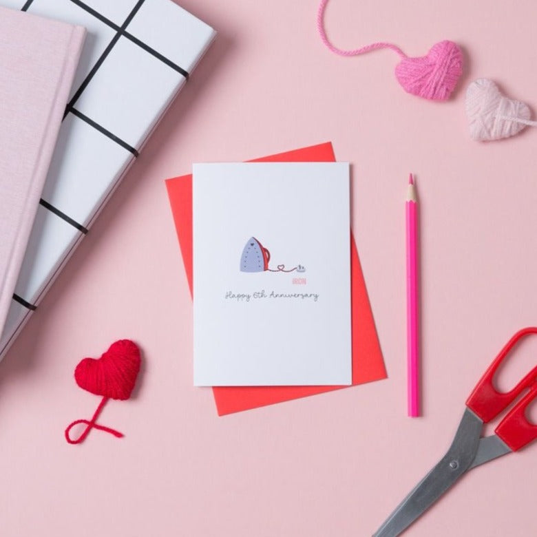A white 6th anniversary card with an illustration of an iron on the front, accompanied by a red envelope. To represent iron, which is the traditional gift for a 6th wedding anniversary.
