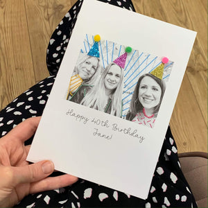 A hand stitched photo card for a 40th birthday. The people in the photo are wearing party hats with colourful pom poms.