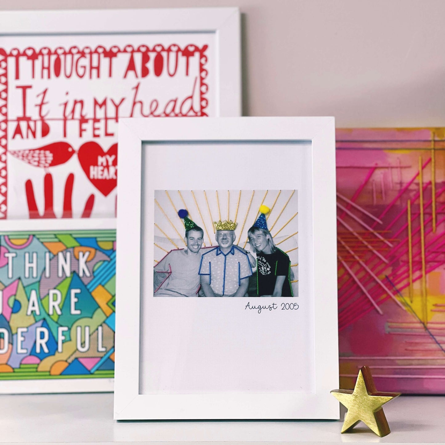 A framed father's day card of a Father and his sons. The picture has been stitched with colourful threads and the people are wearing sparkly hats.