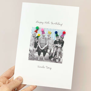 A handmade personalised 70th birthday card. On the card is a photo of a family. They have sparkly party hats on with pom poms