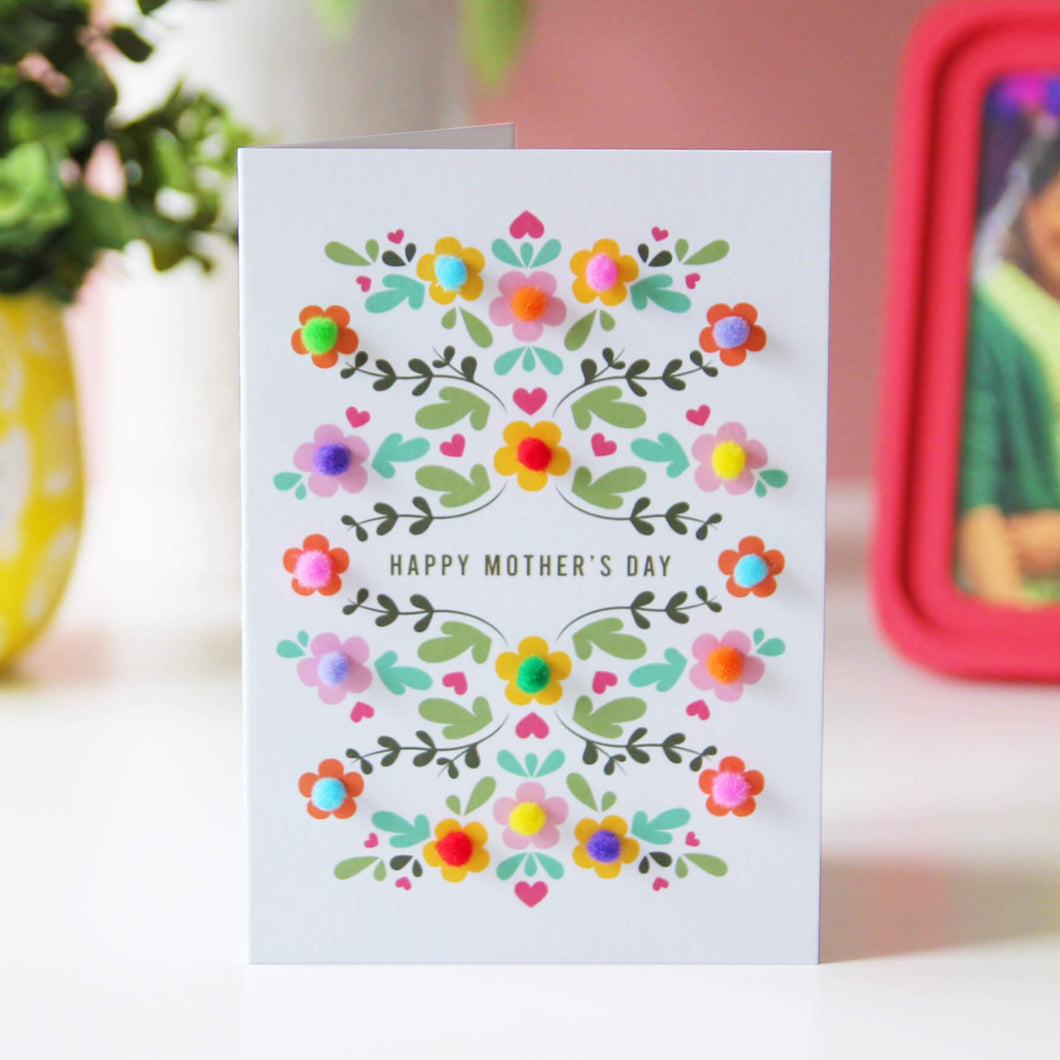 Pom pom flower Mother's day card. The card has a floral pattern and is decorated with colourful little pom poms