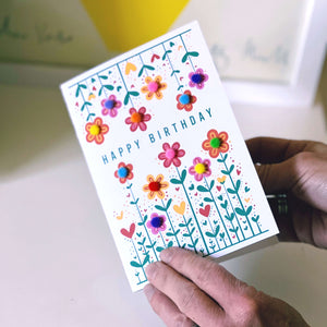 Hands holding a flower birthday card which has been decorated with pom poms