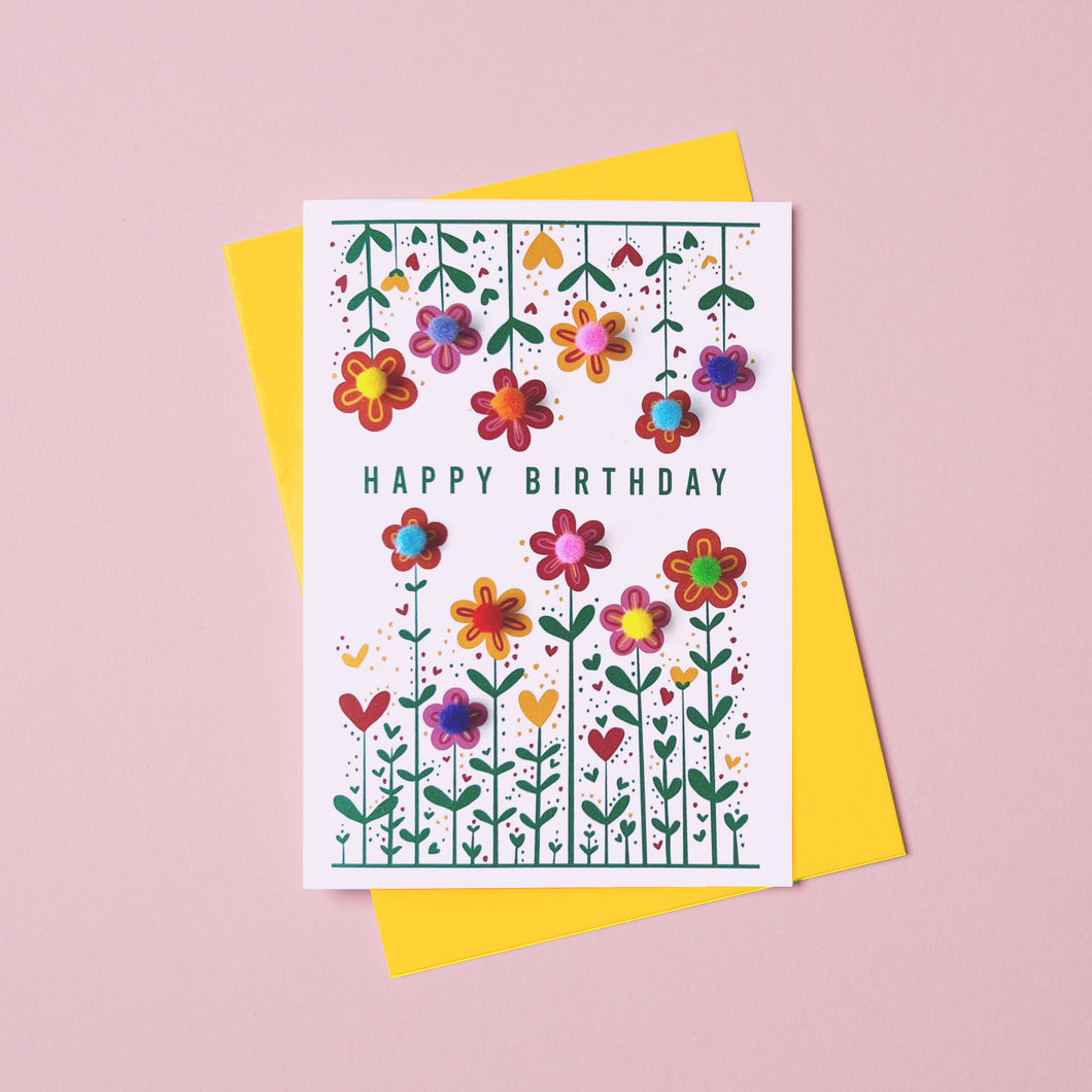 Birthday card with colourful flowers and decorated with pom pom. Th e birthday card says Happy Birthday