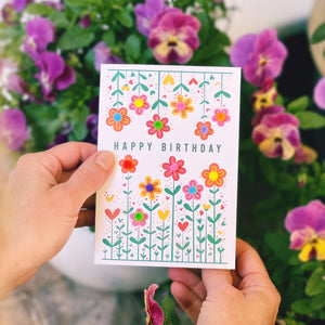 Hands holding a birthday card with colourful pom pom flowers on the front.
